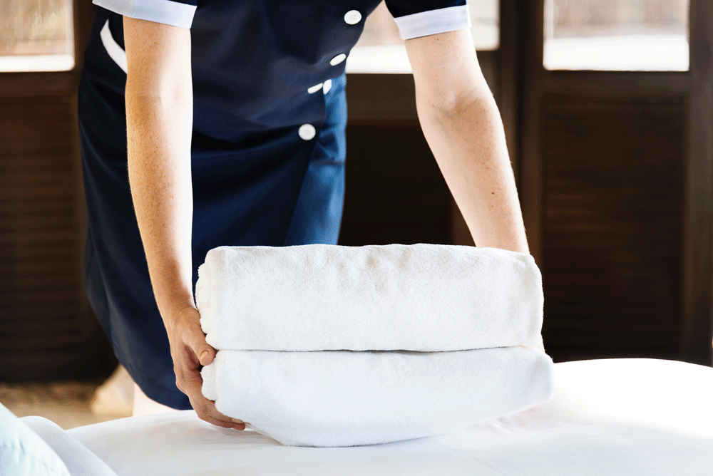 Housekeeper places clean towels on a bed