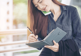 An organized businesswoman writes in her notebook while talking on the telephone