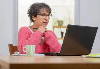 An older job applicant wearing a pink cardigan puts the finishing touches to her resume using a laptop to alter her resume's margins