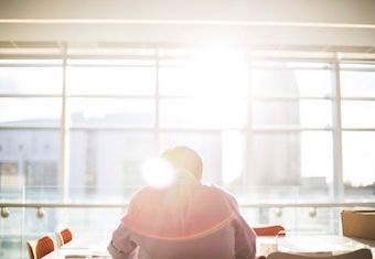 man sitting in front of a large office window with bright sun shining through