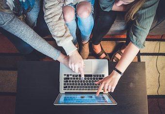 three women sitting on a couch pointing at a laptop