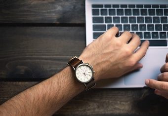 man looking at his time piece while working on his laptop