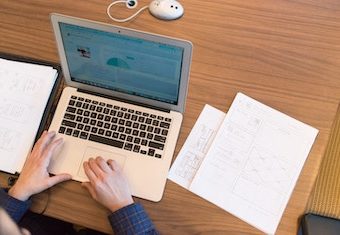 woman sitting at a wooden table writing a functional resume on her laptop with papers next to her