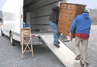 Two people move furniture into a removal van
