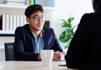 A bespectacled job applicant smiles as he talks during his job interview with an unseen interviewer