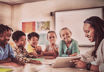 A teacher uses a tablet computer to teach a group of four students in her classroom