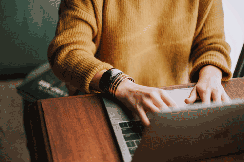 A photo of a person in a warm yellow sweater editing on their laptop.