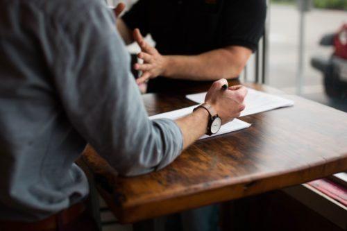 Two men discussing the 10 commandments of writing a resume at a high wooden table